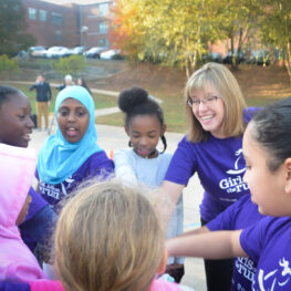 Woman with group of five young girls with hands in a circle ready to celebrate