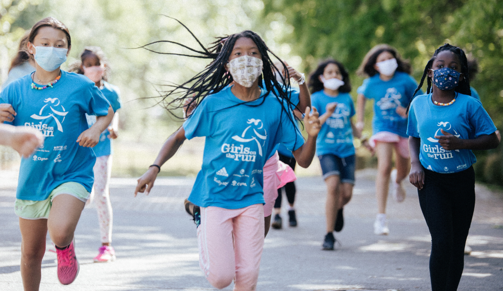 Girls on the Run participants running outside. They are wearing GOTR program shirts. Each girl is unique. The image indicates diversity in culture, ethnicity and accessibility, which shows how the program is welcoming and truly celebrates global diversity awareness.