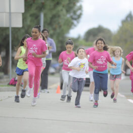 Group of young girls in colorful t-shirts run in 5K event. Like National Family Week, 5Ks bring families together.