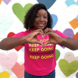 Smiling woman with pink shirt forms a heart shape with her hands; she is happy to work for a best place to work.