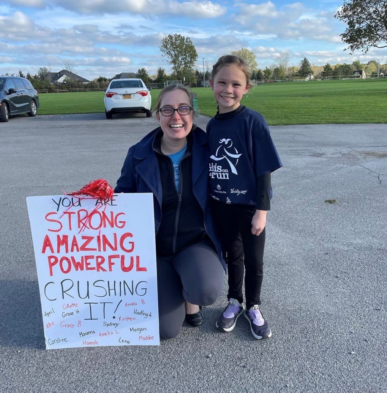 Smiling coach with glasses and smiling girl pose with a fantastic 5K sign that says you are strong, amazing, powerful, crushing it!