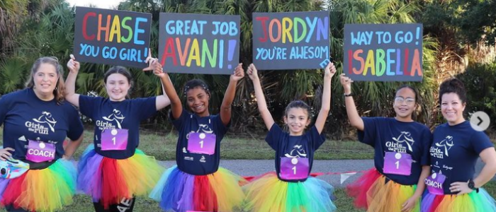 Group of four girls and two coaches wearing rainbow tutus holding up fantastic 5K signs with girls' names