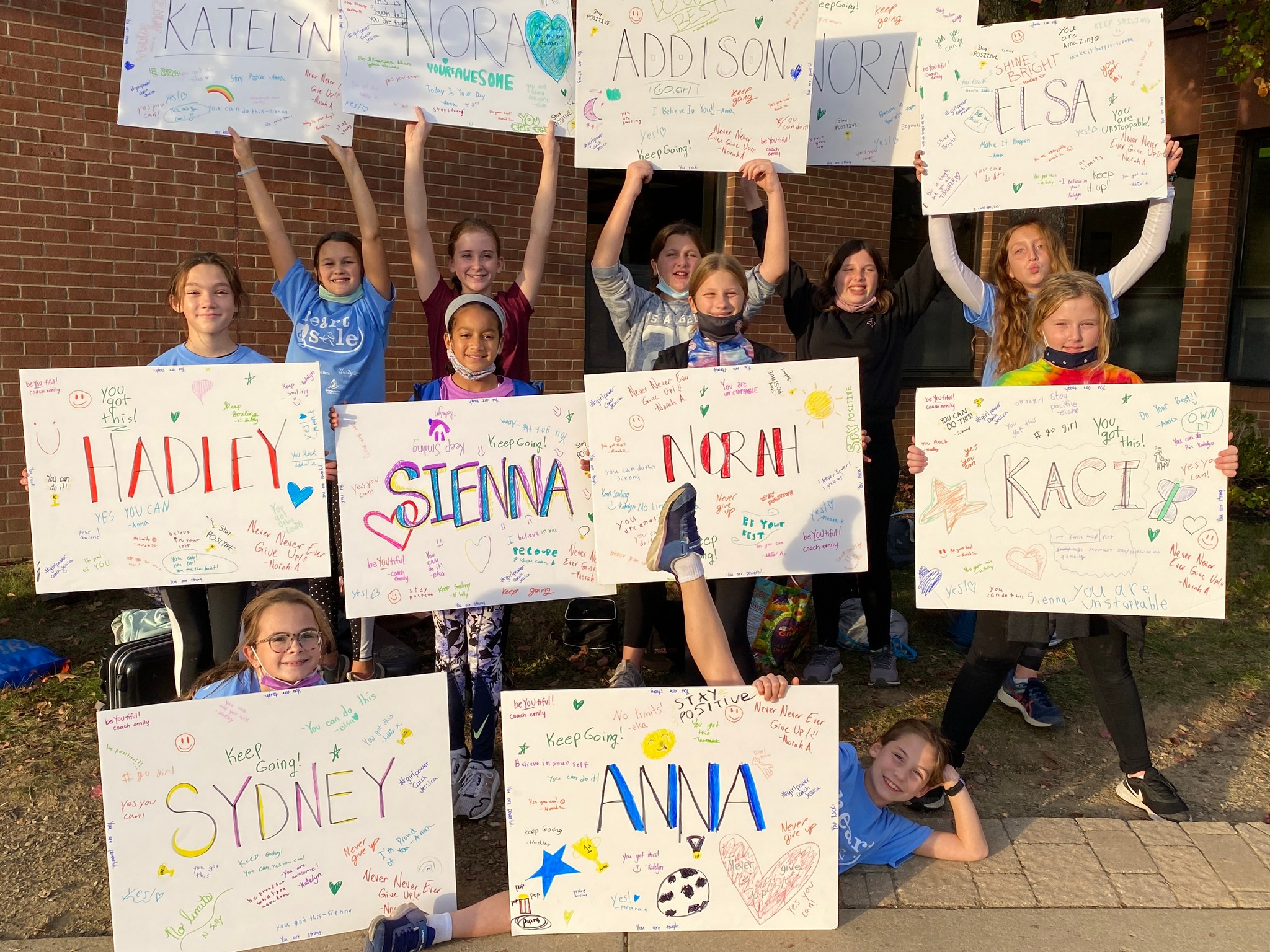 Large group girl girls holding up fantastic 5K signs with teammates' names and custom messages.