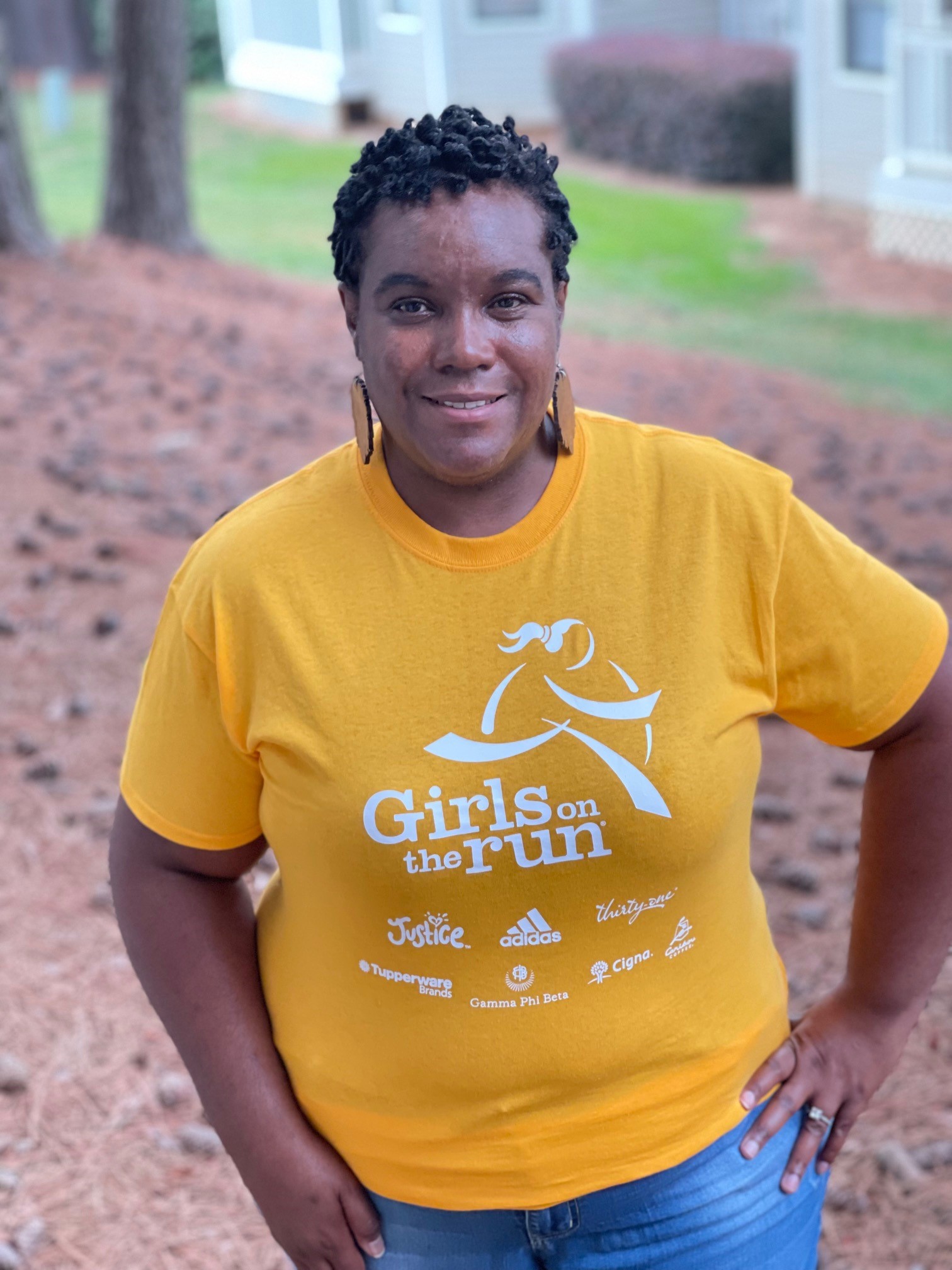 GOTR Coach posing outside wearing a yellow Girls on the Run program shirt