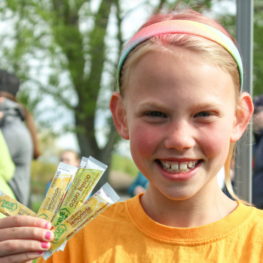 Girl smiling and holding True Citrus products available to purchase to support Girls on the Run