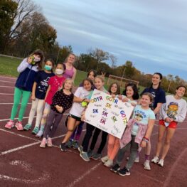 Group of girls and three coaches on track at practice.